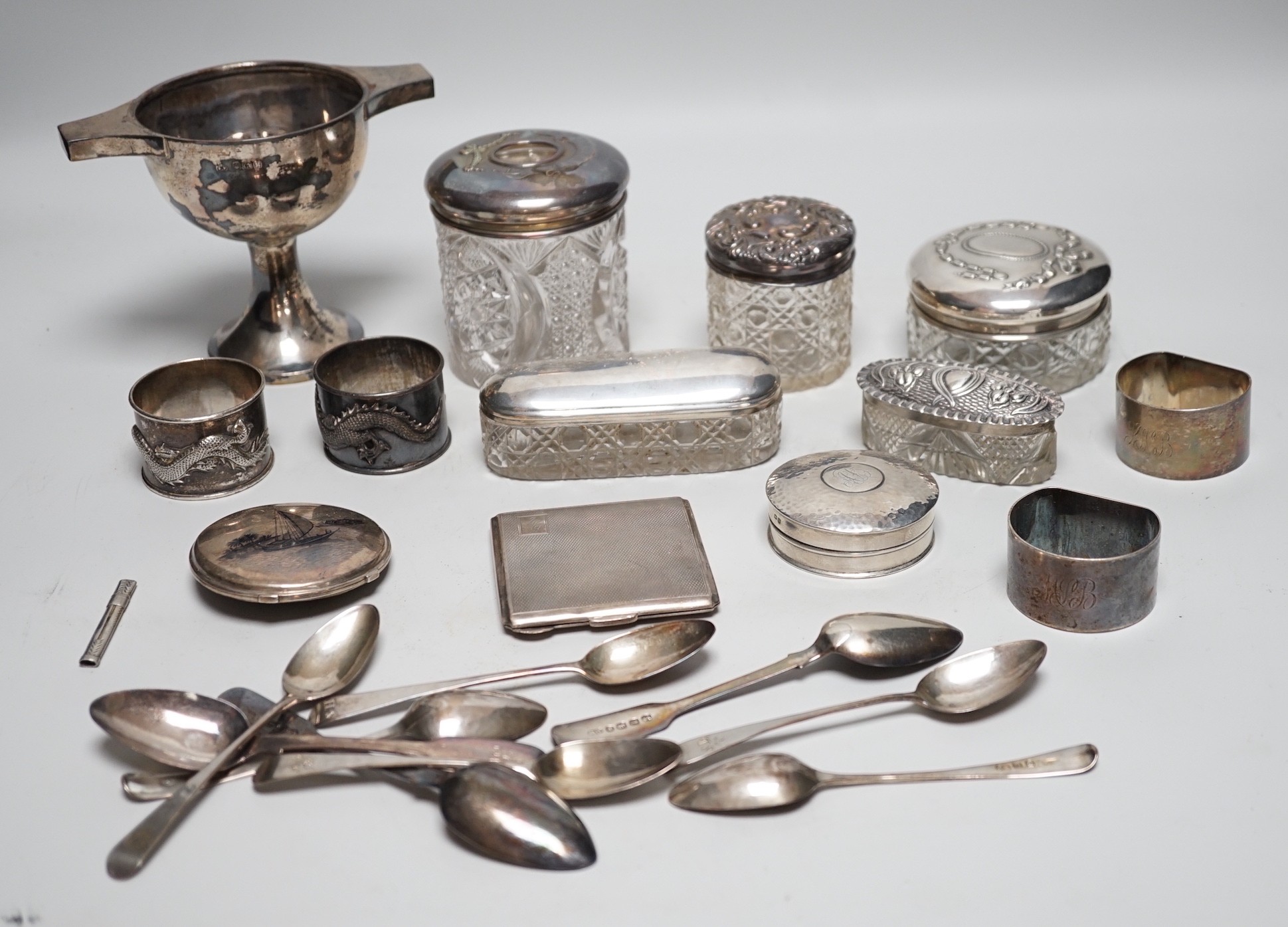 Sundry silver items, including a 1930's silver presentation cup, height 10.9cm, five silver or white metal mounted glass toilet jars, two silver napkin rings, two compacts, silver flatware and two Chinese white metal nap